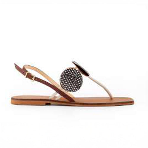 Stylish flat sandal featuring a tan footbed, thin T-straps, and a large round embellishment in black and white polka dots. Set against a white background