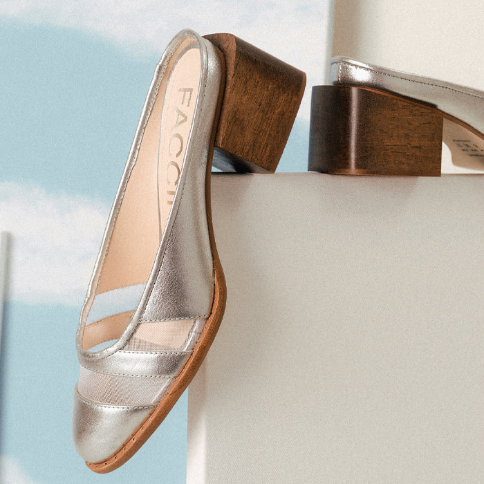 Silver heeled mule shoes resting on a podium, featuring a wooden block heel and a stylish mesh panel design.